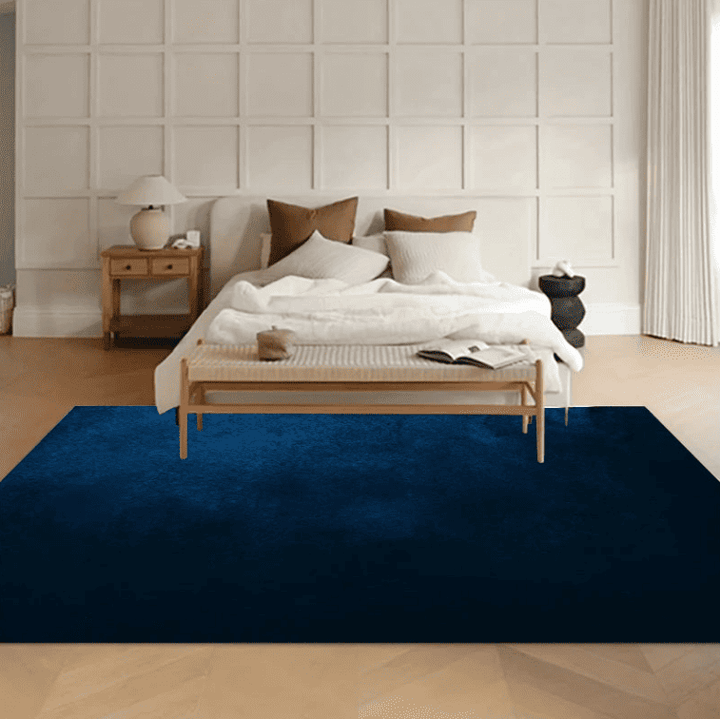 Tapis salon bleu marine doux placé au pied d'un lit dans une chambre élégante et lumineuse.