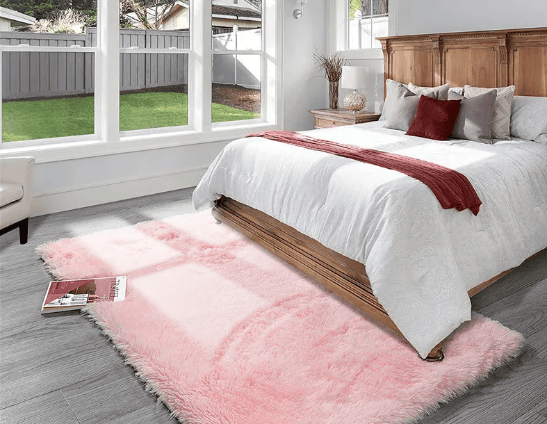Tapis rose moelleux et doux placé au pied d'un lit en bois dans une chambre lumineuse avec sol en parquet gris.