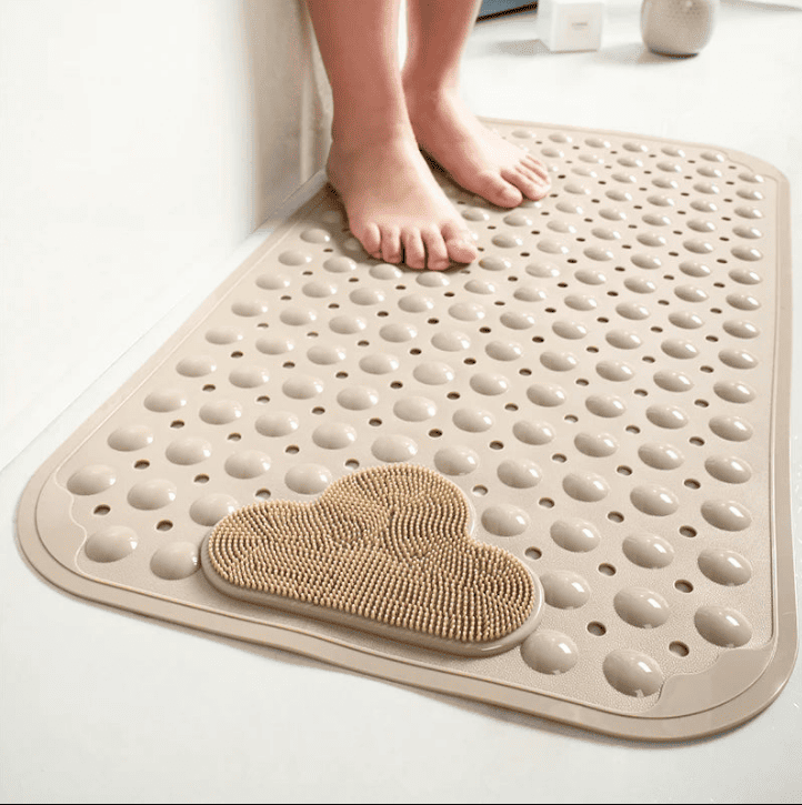 Tapis de bain antidérapant beige avec picots massants et perforations, pieds posés dessus dans une salle de bain épurée.