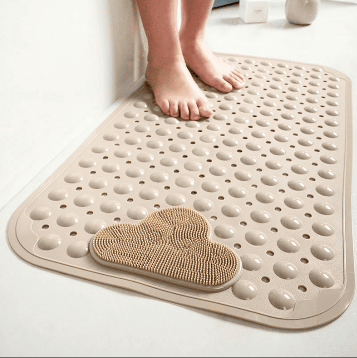 Tapis de bain antidérapant beige avec picots massants et perforations, pieds posés dessus dans une salle de bain épurée.