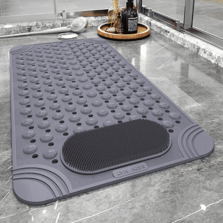 Tapis de bain antidérapant gris à picots et surface massante, posé sur un sol carrelé près d’une douche avec accessoires de toilette.