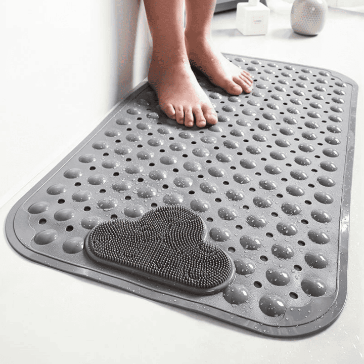 Tapis de bain antidérapant gris à picots et perforations pour un séchage rapide, pieds posés dessus dans une salle de bain moderne.