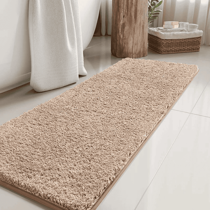 Tapis de bain long beige en fibres douces devant une baignoire blanche, idéal pour absorber l’eau et apporter chaleur et élégance à votre salle de bain.