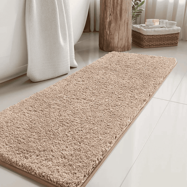 Tapis de bain long beige en fibres douces devant une baignoire blanche, idéal pour absorber l’eau et apporter chaleur et élégance à votre salle de bain.