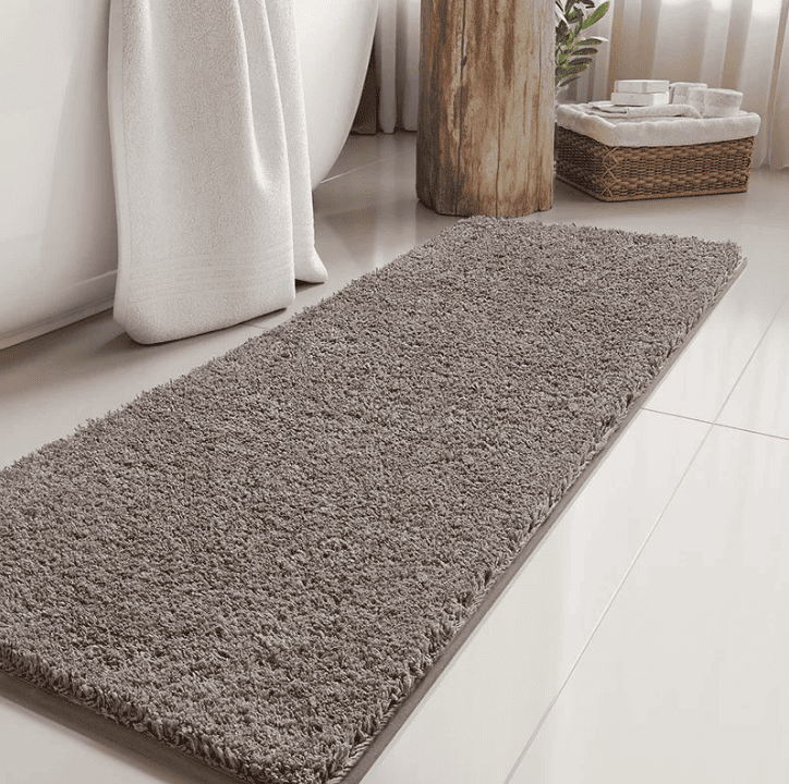 Tapis de bain long marron foncé en fibres moelleuses placé devant une baignoire blanche, apportant confort et élégance à une salle de bain moderne lumineuse.
