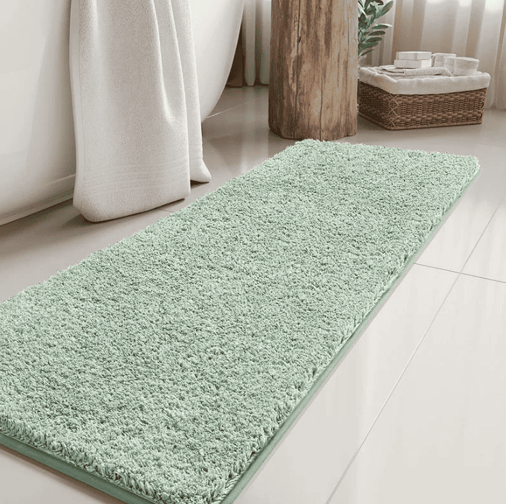 Tapis de bain long vert menthe moelleux disposé devant une baignoire, créant une ambiance cocooning et moderne dans une salle de bain lumineuse.