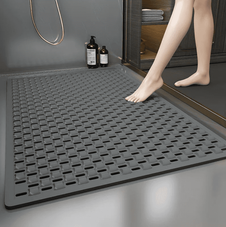 Personne âgée posant délicatement son pied sur un grand tapis de bain antidérapant gris, conçu pour sécuriser la sortie de la douche et éviter les chutes.
