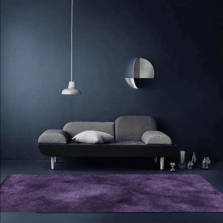 Tapis salon violet uni installé dans un salon moderne avec une décoration élégante et une ambiance chaleureuse.