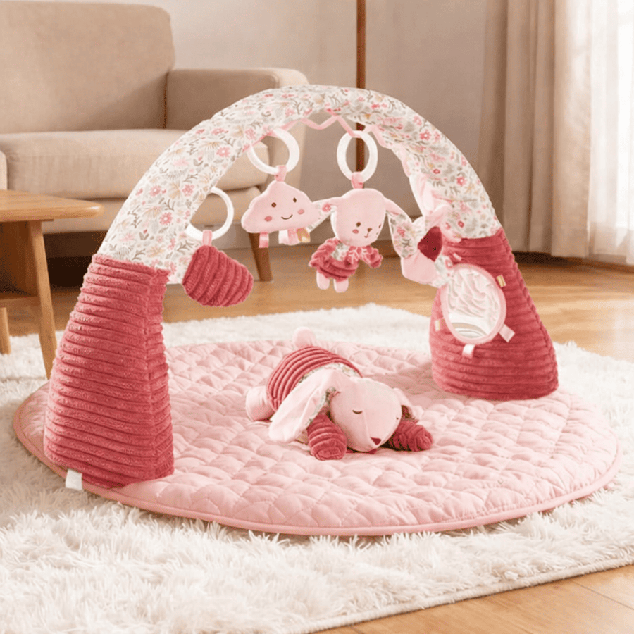 Tapis d’éveil bébé rose avec arche fleurie, jouets suspendus et coussin moelleux dans un salon
