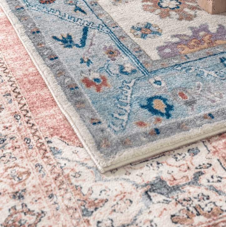 Salon contemporain avec un tapis oriental vintage rose poudré aux motifs floraux, posé sur un parquet sombre devant un canapé gris.