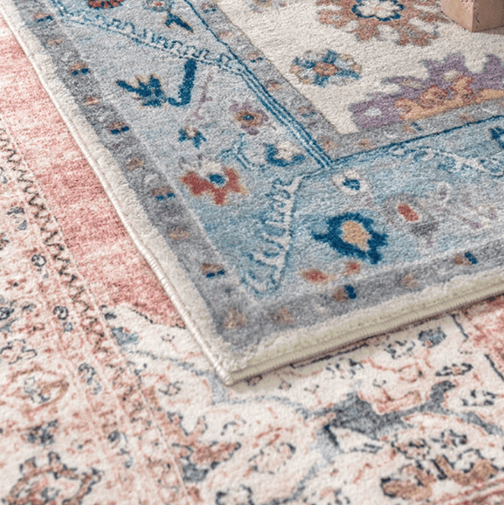 Salon contemporain avec un tapis oriental vintage rose poudré aux motifs floraux, posé sur un parquet sombre devant un canapé gris.