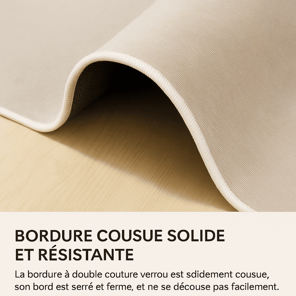 Gros plan d’un coin de tapis beige replié, révélant son dessous gris foncé. La bordure est finement cousue en double surpiqûre