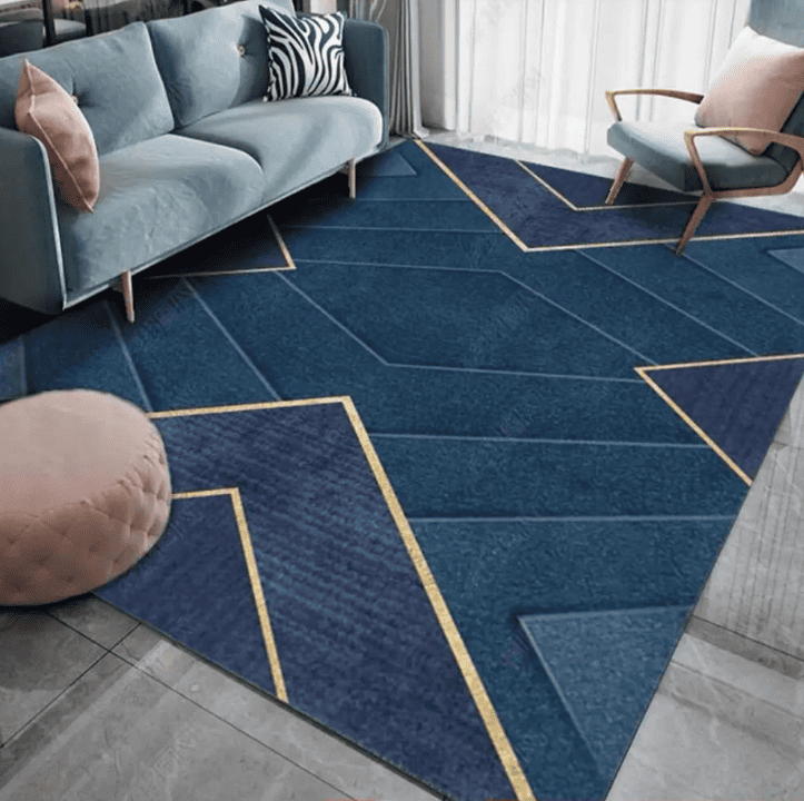 apis de salon grand format bleu avec motif géométrique et liserés dorés, installé sous un canapé et un fauteuil dans une pièce lumineuse.