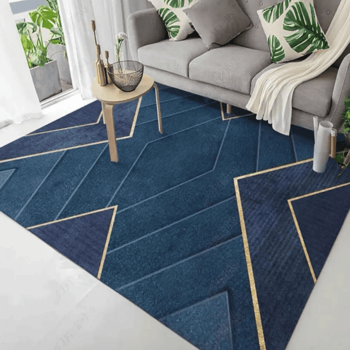 Tapis de salon bleu profond à motif géométrique avec lignes dorées, posé sous une table basse devant un canapé gris dans un intérieur lumineux.