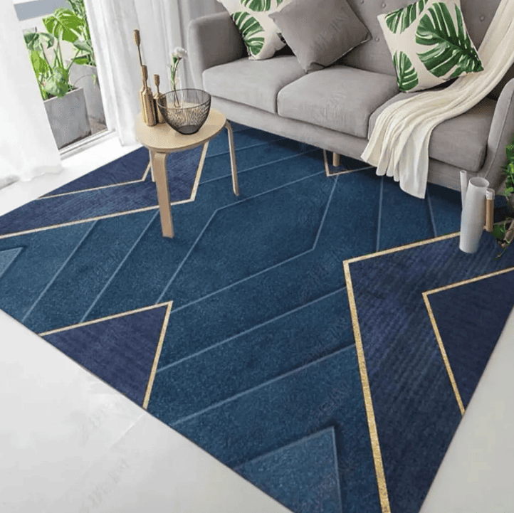 Tapis de salon bleu profond à motif géométrique avec lignes dorées, posé sous une table basse devant un canapé gris dans un intérieur lumineux.