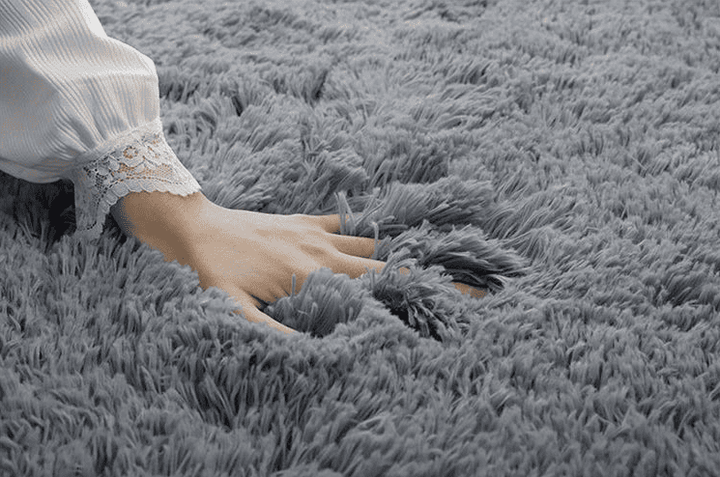 Main enfoncée dans un tapis gris moelleux au salon, illustrant la douceur et le confort du tissu.
