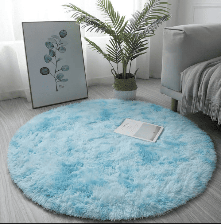 Tapis rond bleu ciel à poils longs, installé dans un salon lumineux près d’un canapé et d’un cadre végétal.