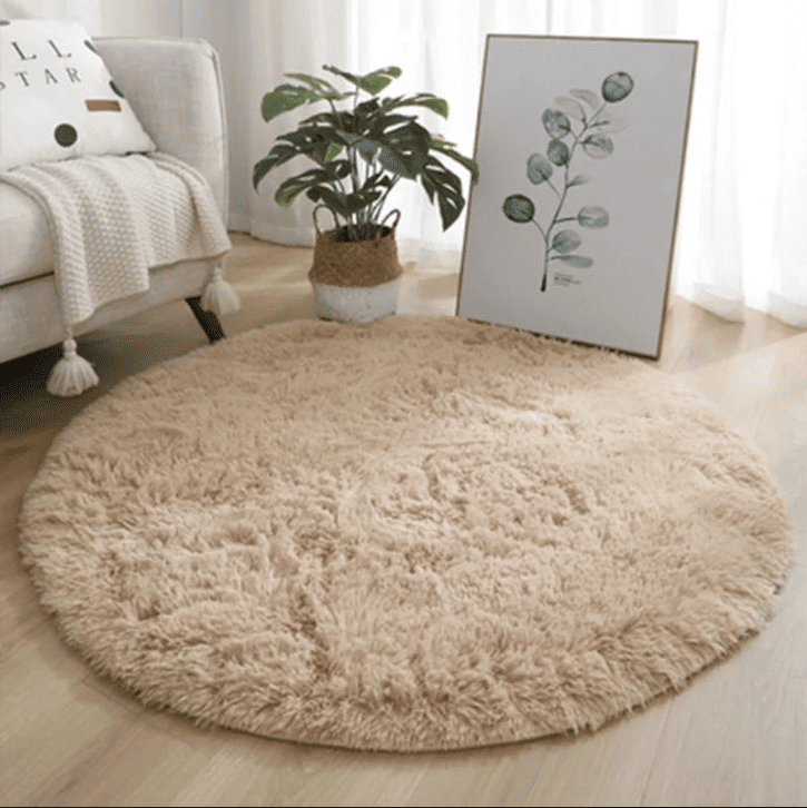 Tapis rond beige à poils longs dans un salon lumineux, placé près d’un canapé et d’une plante décorative.