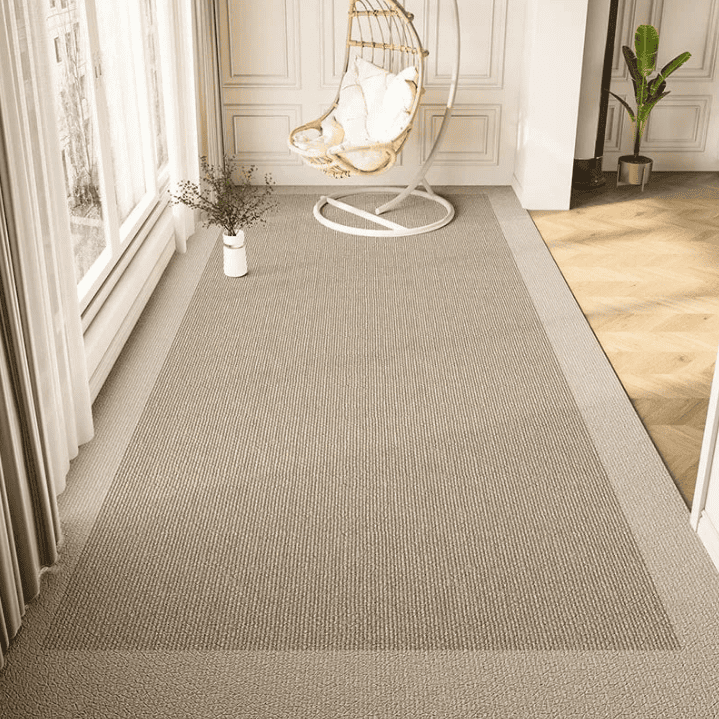 Un salon lumineux avec un grand tapis taupe à bordure légèrement plus claire, posé sur un parquet clair