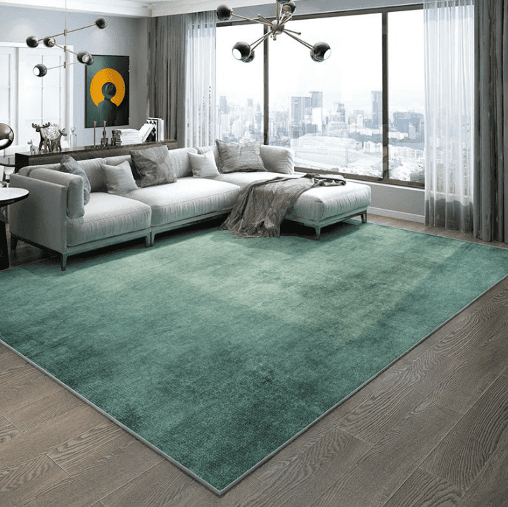 Tapis vert 200×300 cm installé dans un salon moderne avec canapé d’angle, grandes fenêtres et parquet en bois foncé.