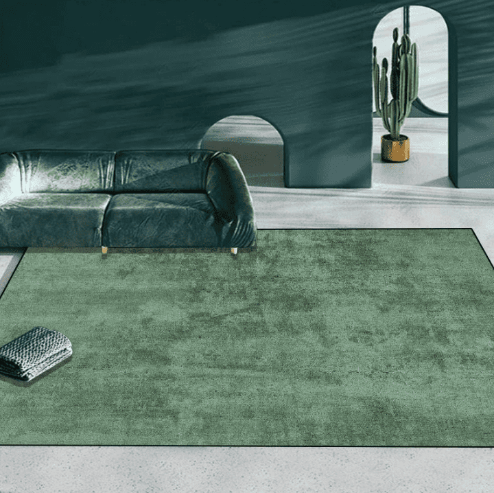 Tapis de salon uni vert posé devant un canapé vert émeraude dans un intérieur moderne avec mur sombre et plante cactus.