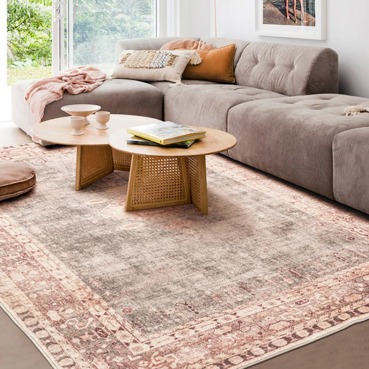 Salon scandinave avec canapé gris et fauteuil en cuir, décor rehaussé d’un tapis vintage oriental rose et beige à motif central géométrique.
